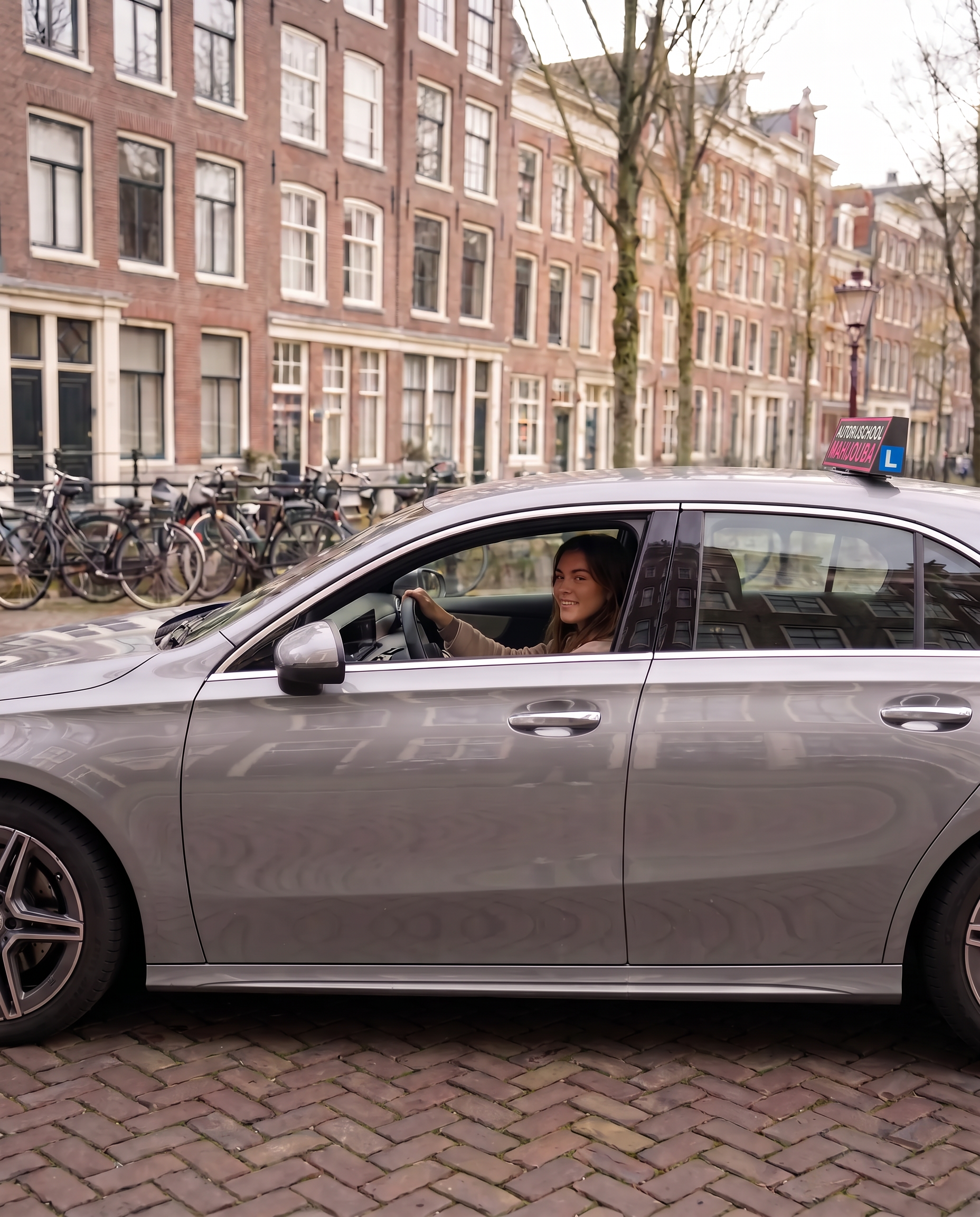 Jonge vrouwelijke rijlesleerling achter het stuur van een Mercedes A-Klasse tijdens een rijles in Amsterdam